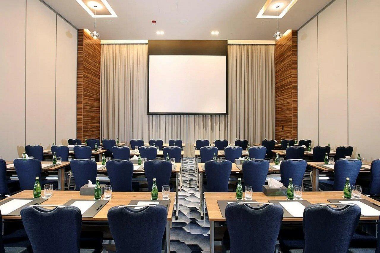 โรงแรมแกรนด์ คอสโมโพลิตัน - ดูไบ ภายนอก รูปภาพ The photo shows a conference room set up for a meeting or presentation. There are several rows of tables arranged in a classroom style, each equipped with blue chairs. On each table, there are notepads and pens, and bottles of water are available for