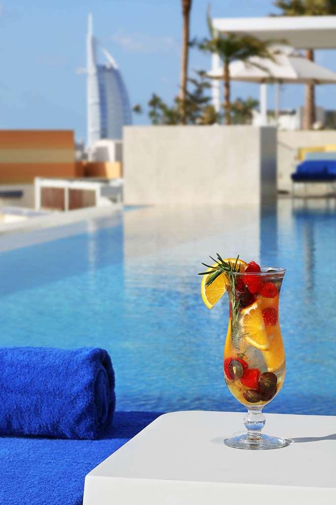 โรงแรมแกรนด์ คอสโมโพลิตัน - ดูไบ สิ่งอำนวยความสะดวก รูปภาพ The photo shows a refreshing cocktail placed on the edge of a pool. The drink is garnished with slices of lemon, raspberries, and possibly some herbs, and is served in a tall glass. In the background, there is a clear blue water surface of the pool, 