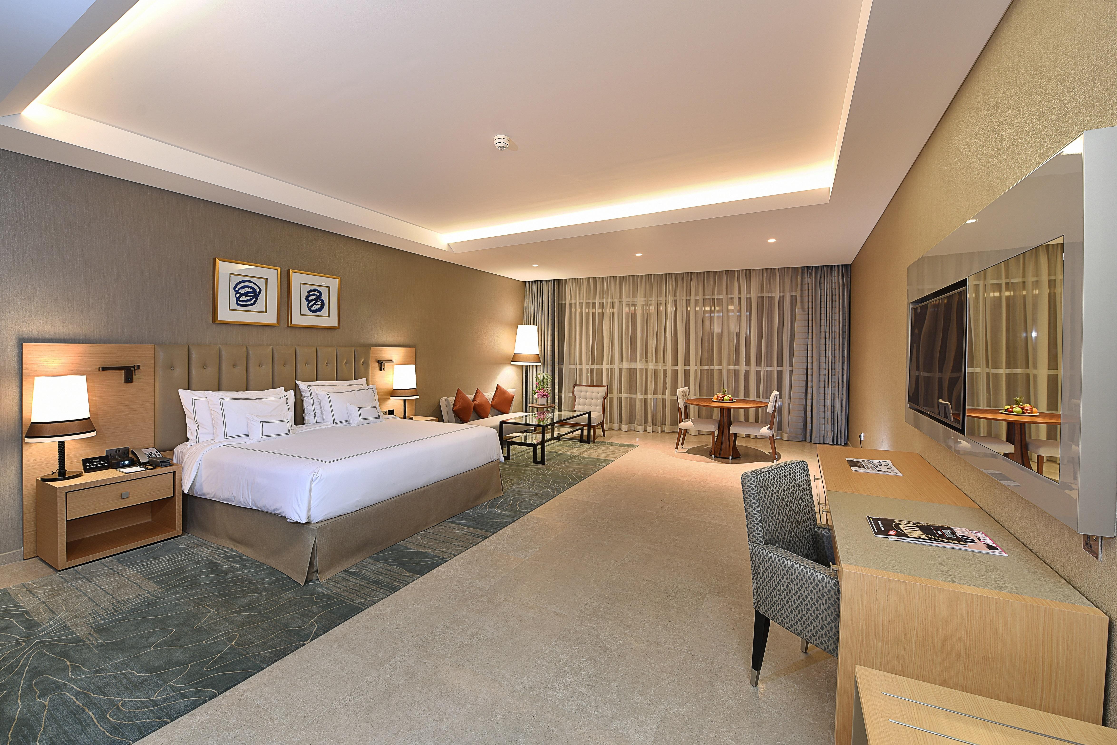 โรงแรมแกรนด์ คอสโมโพลิตัน - ดูไบ ภายนอก รูปภาพ The photo shows a modern hotel room. It features a spacious layout with a large bed, complemented by bedside tables and lamps. There's a comfortable seating area with two chairs and a small table. A desk with a chair is positioned against one wall, a