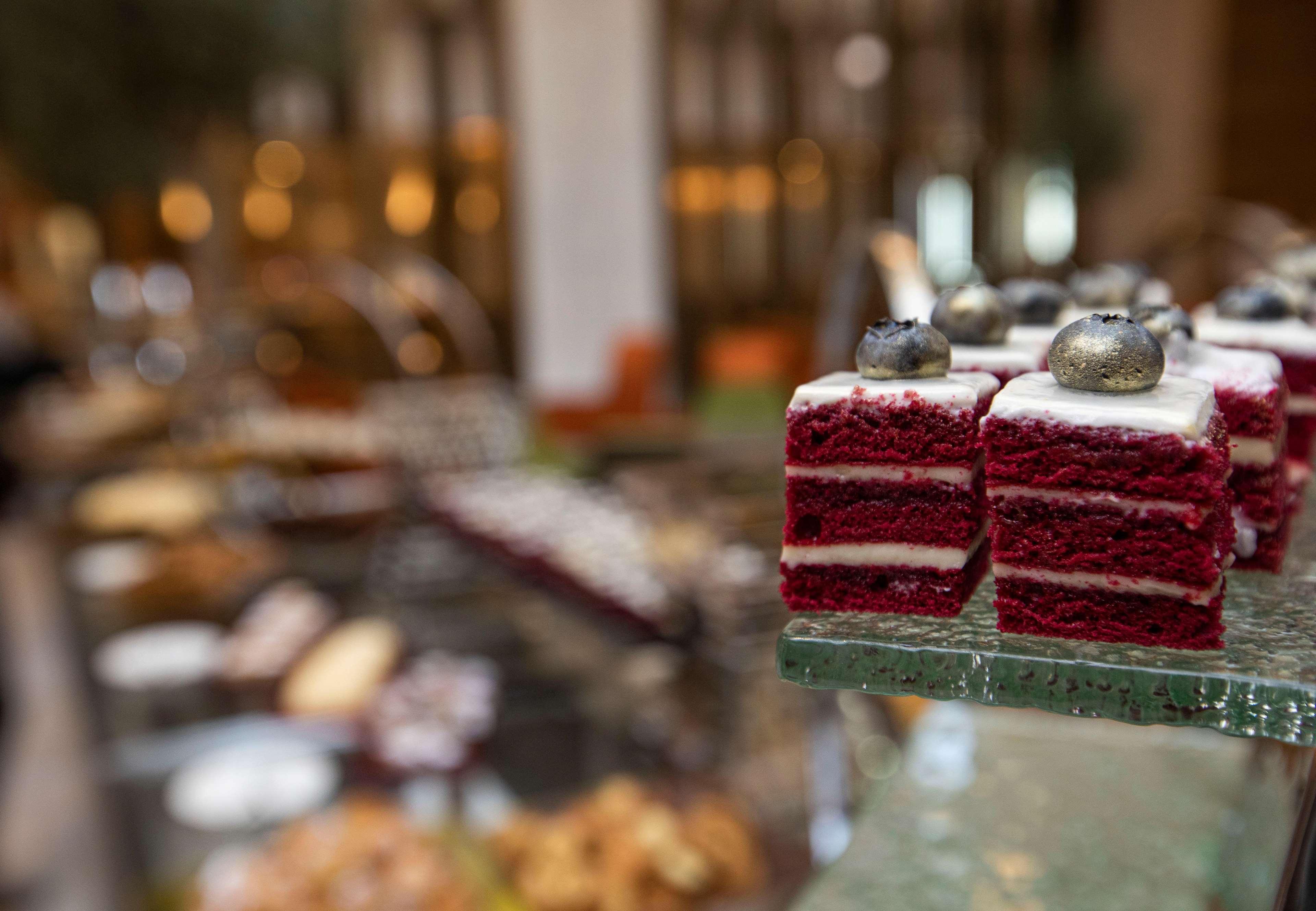 โรงแรมแกรนด์ คอสโมโพลิตัน - ดูไบ ภายนอก รูปภาพ The photo showcases a selection of desserts, with a particular focus on red velvet cake squares. The cake pieces are layered, featuring a rich red color and topped with a small decoration. In the background, there are various other desserts and pastr