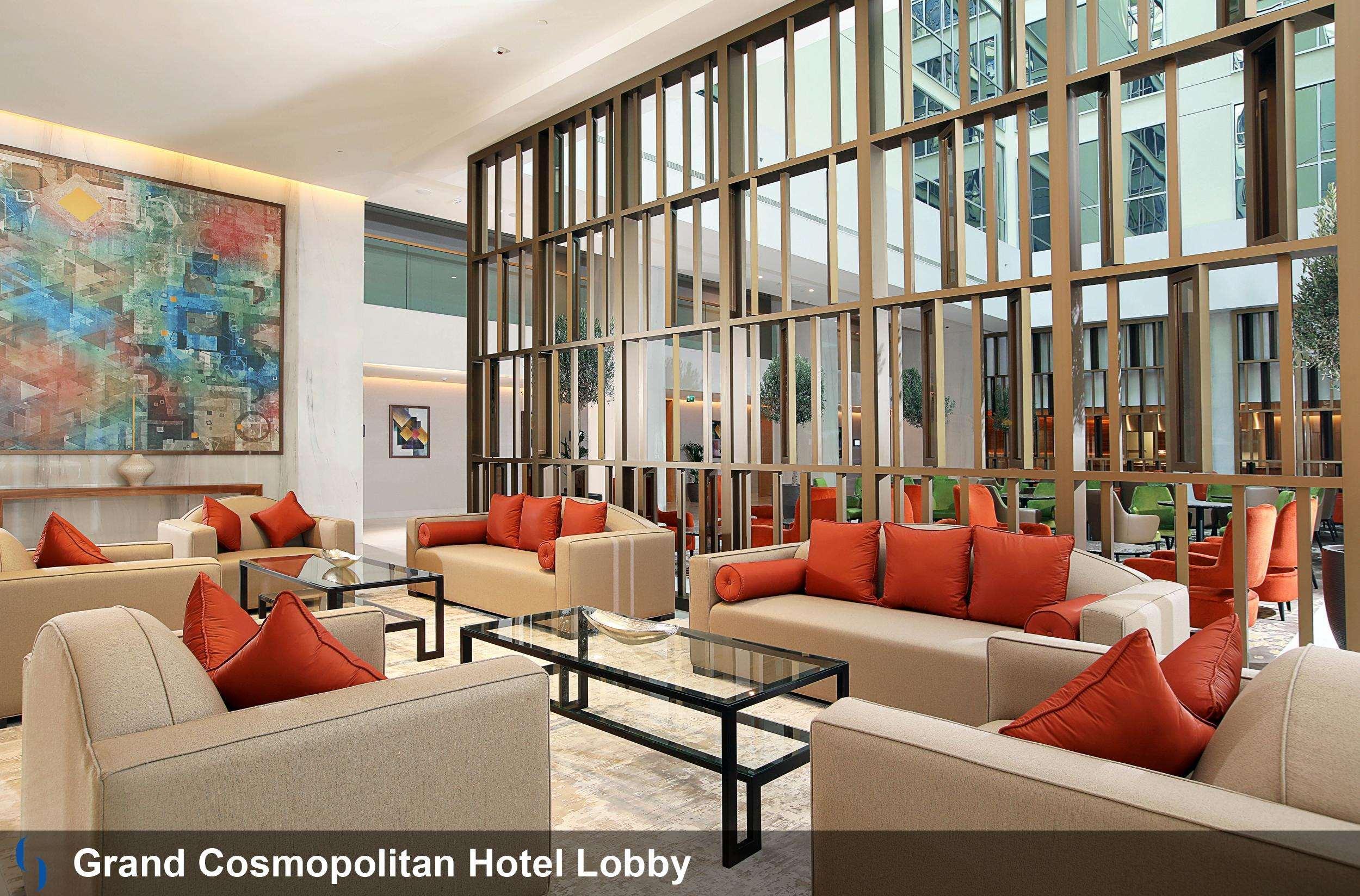 โรงแรมแกรนด์ คอสโมโพลิตัน - ดูไบ ภายนอก รูปภาพ The image shows the lobby of the Grand Cosmopolitan Hotel. The space features a modern and stylish design, with beige sofas and bright orange cushions arranged around glass coffee tables. There are decorative elements such as a large abstract paintin