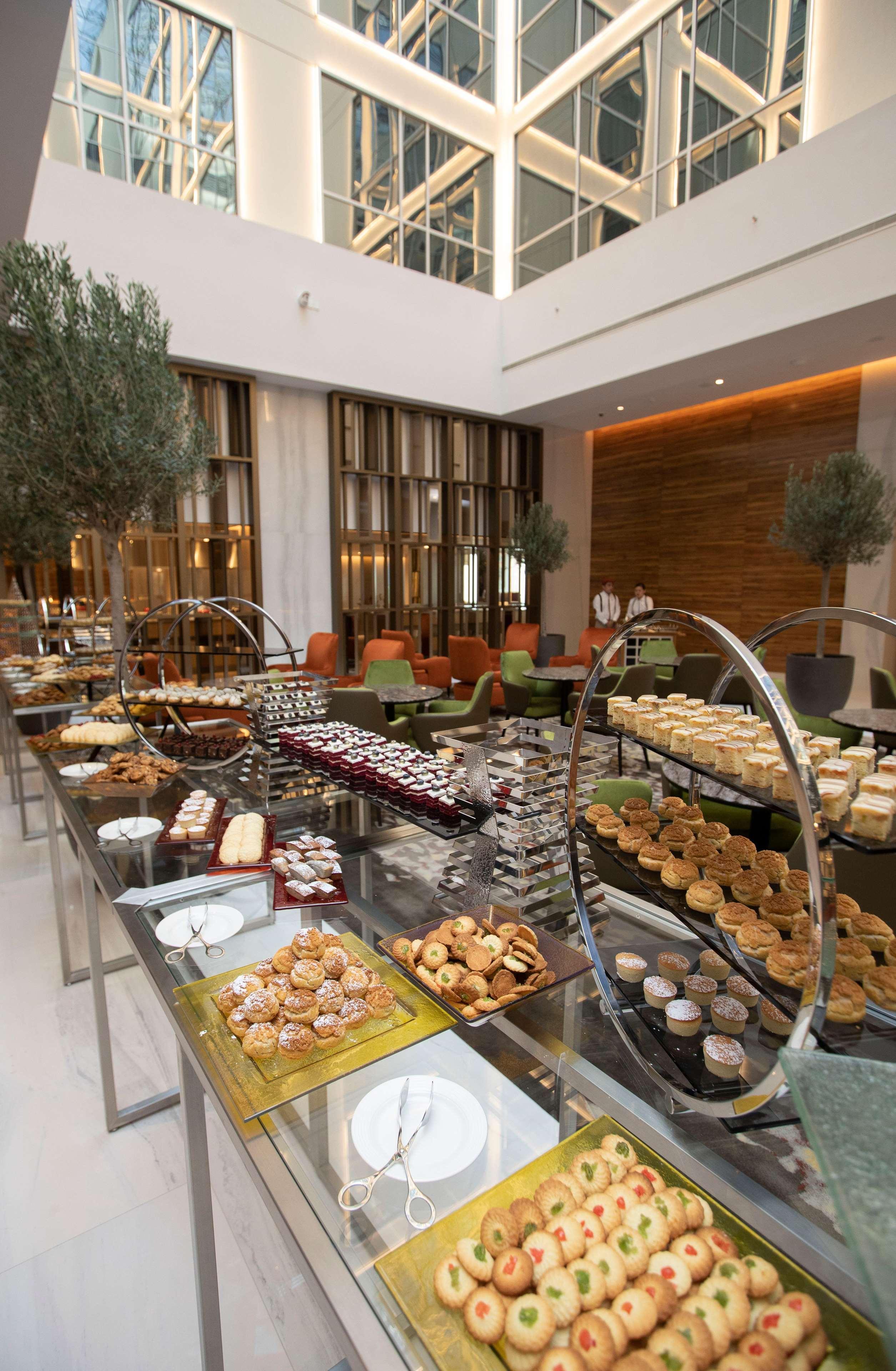 โรงแรมแกรนด์ คอสโมโพลิตัน - ดูไบ ภายนอก รูปภาพ The photo depicts a beautifully arranged dessert buffet in a modern setting. Various types of pastries and sweets are displayed on elegant stands and tables. You can see an assortment of items, including cakes, tarts, cookies, and small desserts, app