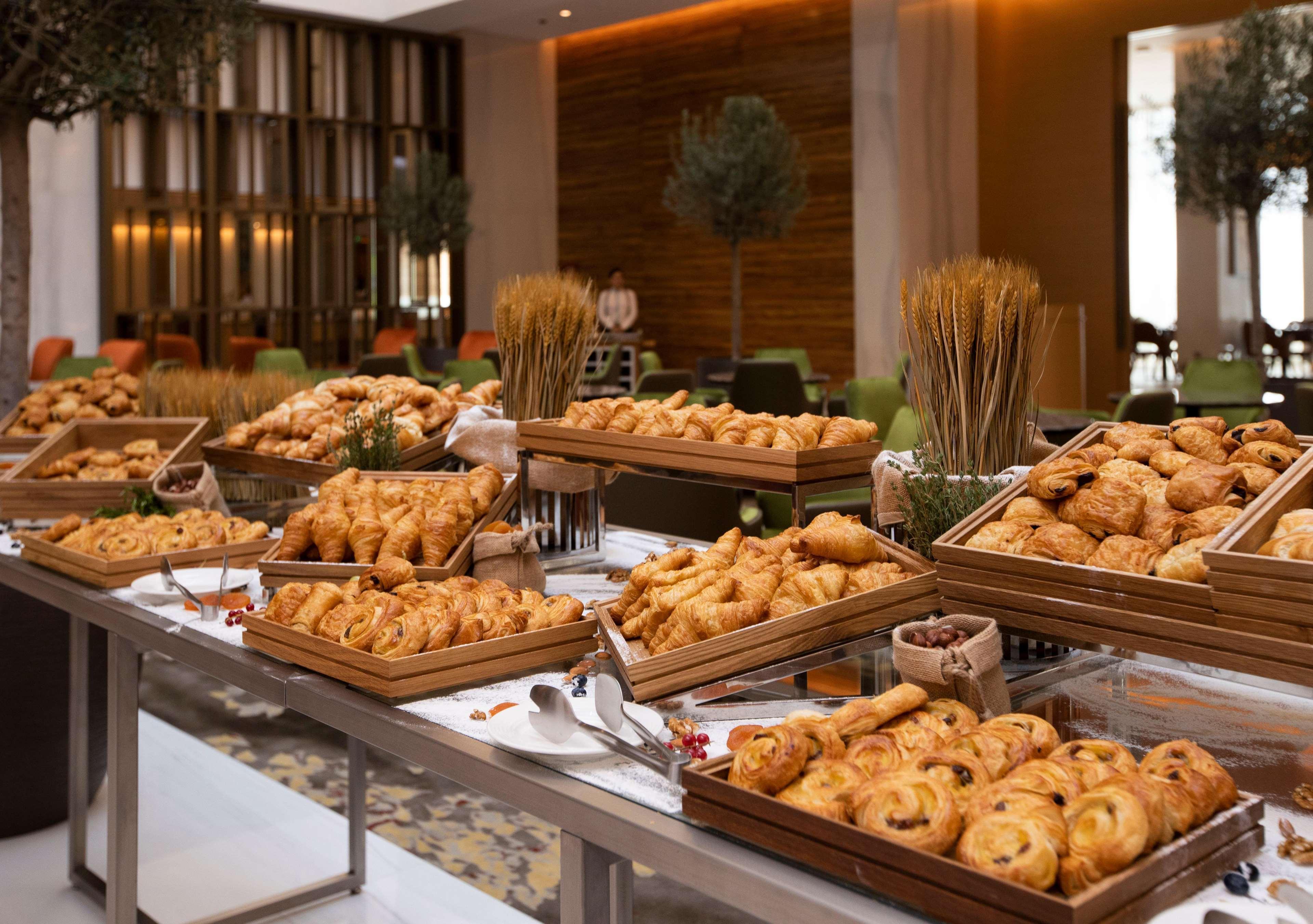 โรงแรมแกรนด์ คอสโมโพลิตัน - ดูไบ ภายนอก รูปภาพ The photo shows a lavish spread of baked goods laid out on a table in a buffet setting. There are various trays filled with an assortment of pastries, including croissants, danishes, and other types of bread. The presentation is appealing, with the p
