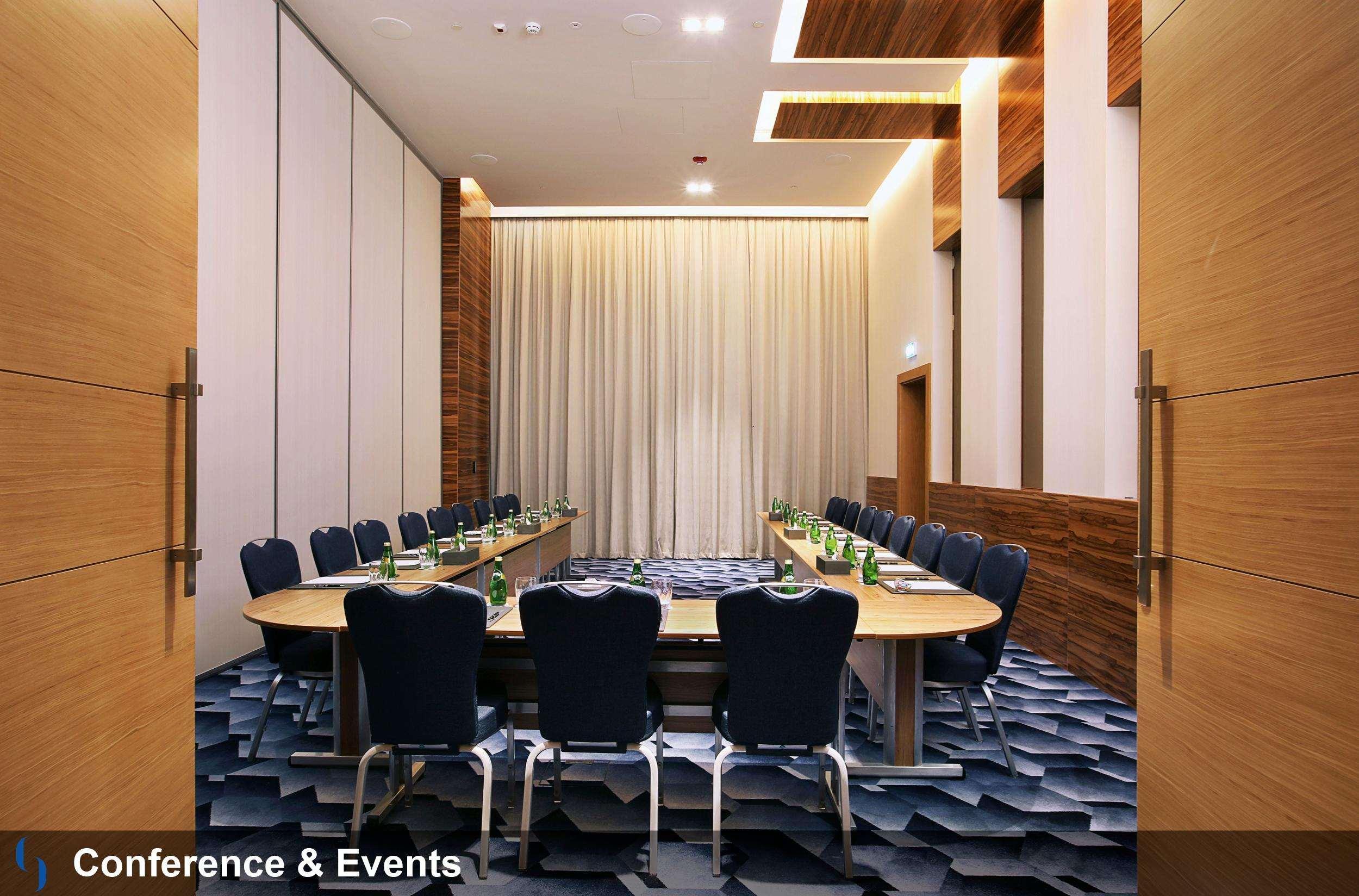 โรงแรมแกรนด์ คอสโมโพลิตัน - ดูไบ ภายนอก รูปภาพ The photo shows an elegantly designed conference room. It features a large, rectangular table surrounded by ergonomic chairs, primarily in a dark blue color. The room has wooden accents on the walls, paired with light-colored curtains. The flooring a