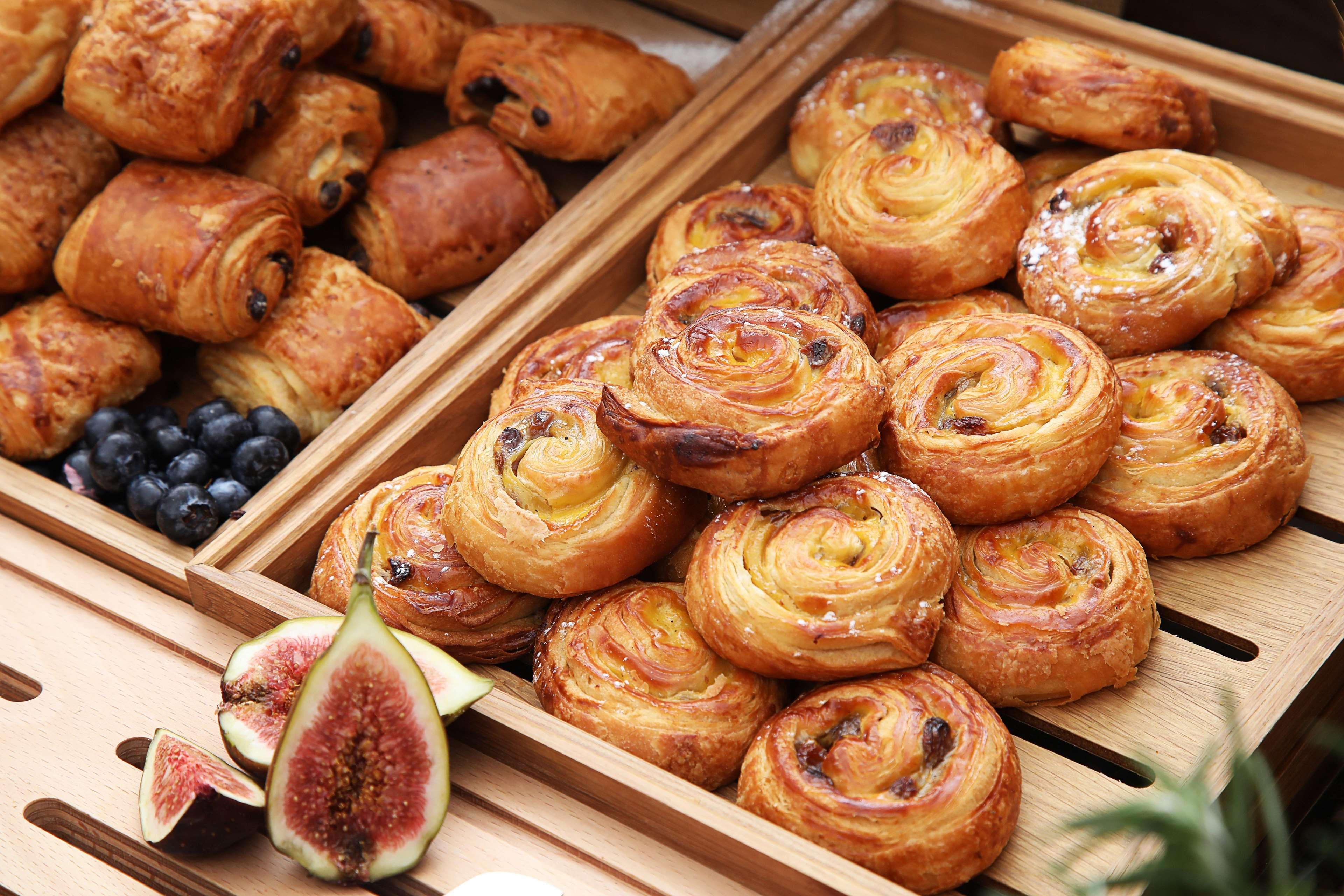 โรงแรมแกรนด์ คอสโมโพลิตัน - ดูไบ ภายนอก รูปภาพ The photo showcases a selection of baked goods, primarily featuring various types of pastries. In one wooden tray, there are spiral-shaped pastries, likely danishes or cinnamon rolls, characterized by a golden-brown color and a flaky texture. Some of
