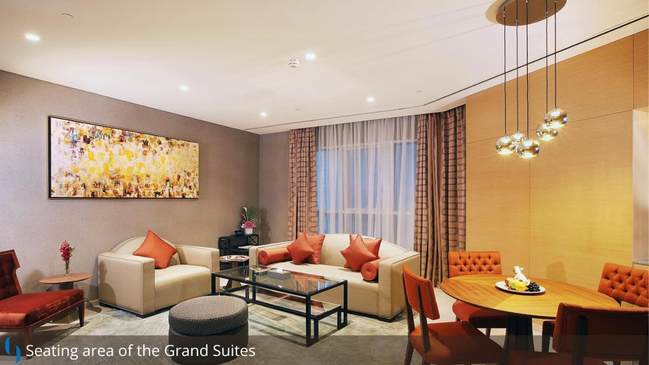 โรงแรมแกรนด์ คอสโมโพลิตัน - ดูไบ ภายนอก รูปภาพ The photo depicts a stylish and modern living area within a suite. There is a light-colored sofa with decorative cushions, a glass coffee table in the center, and a cozy armchair nearby. To the side, there is a small round dining table with four chai