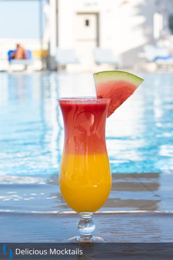 โรงแรมแกรนด์ คอสโมโพลิตัน - ดูไบ ภายนอก รูปภาพ The image features a colorful drink in a tall glass. The beverage has a gradient effect, with vibrant red at the top gradually transitioning to a bright yellow at the bottom. A slice of watermelon is perched on the rim of the glass, adding a decorati