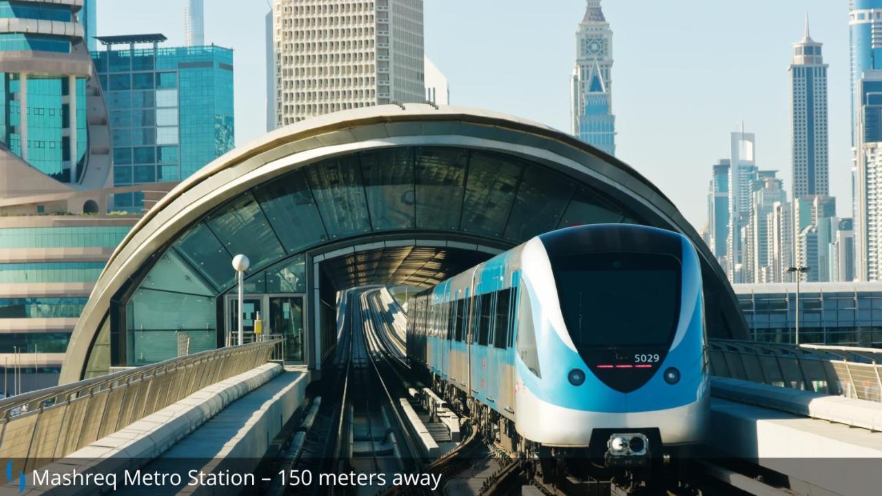 โรงแรมแกรนด์ คอสโมโพลิตัน - ดูไบ ภายนอก รูปภาพ The photo shows a modern metro train approaching a station, with a distinctive curved structure overhead that forms part of the station's design. The scene appears to be set in a city with tall skyscrapers in the background, indicating an urban envir