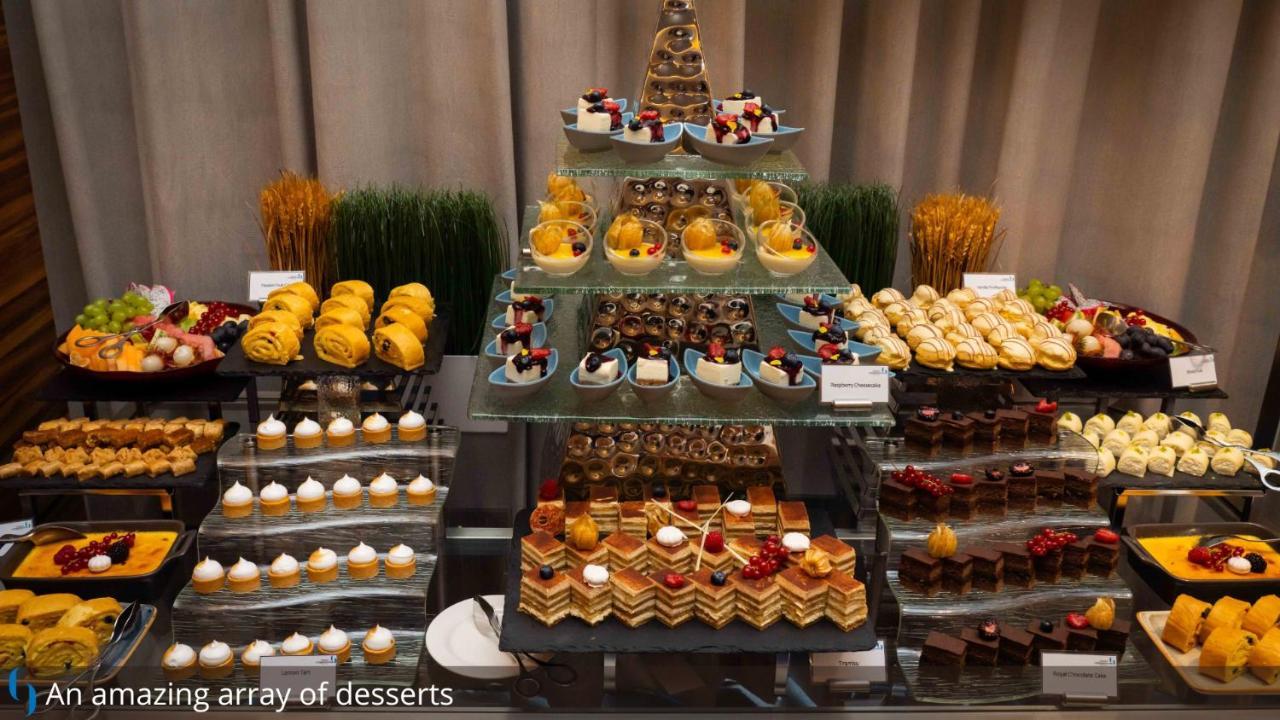 โรงแรมแกรนด์ คอสโมโพลิตัน - ดูไบ ภายนอก รูปภาพ The photo showcases an impressive assortment of desserts arranged elegantly. There are multiple tiers of sweets, including small pastries, cakes, and colorful treats. The display features a variety of chocolate-covered items, fruit-topped desserts, a