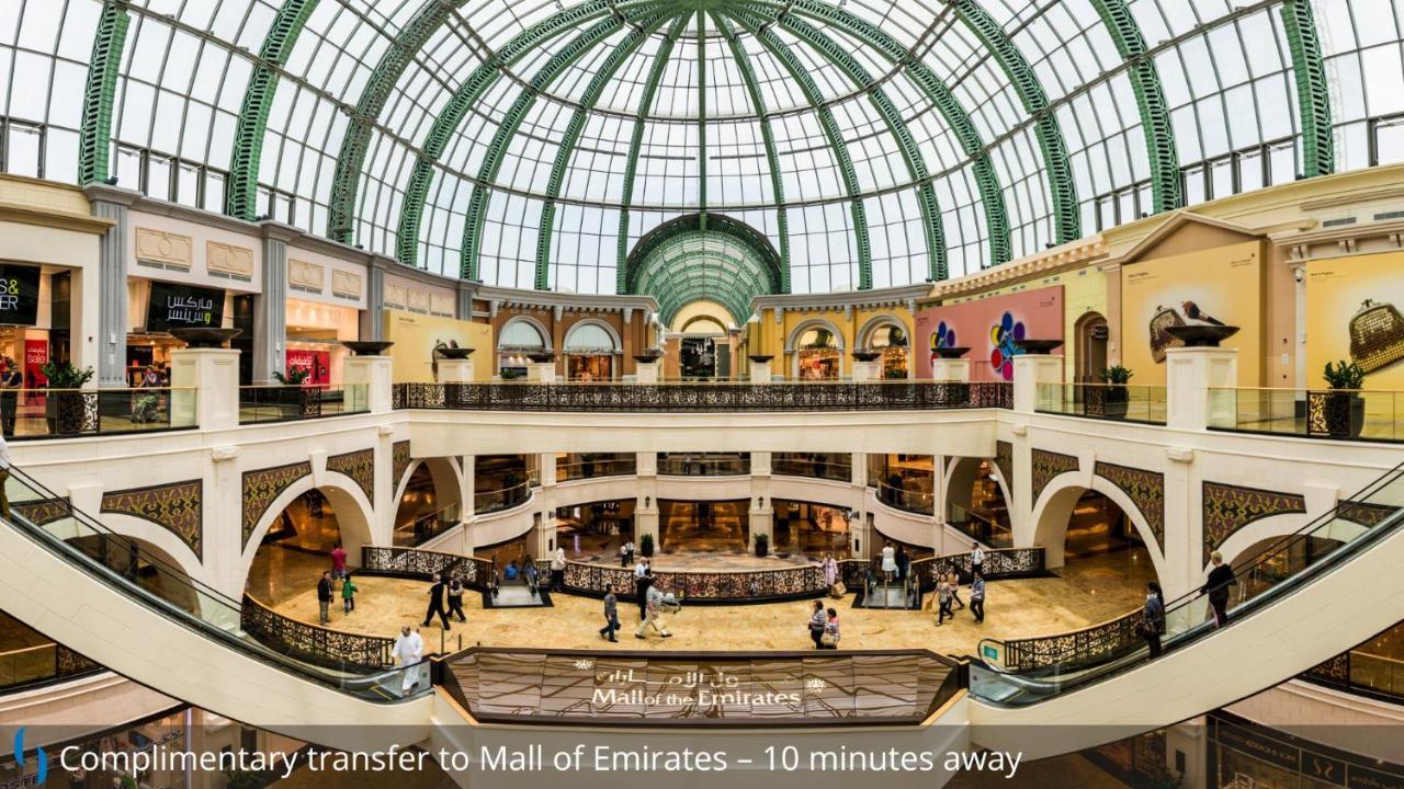 โรงแรมแกรนด์ คอสโมโพลิตัน - ดูไบ ภายนอก รูปภาพ The photo shows the interior of a large shopping mall, featuring an expansive, open layout with multiple levels. There is a stunning glass dome ceiling that allows natural light to illuminate the space, highlighting the luxurious architecture. The ar