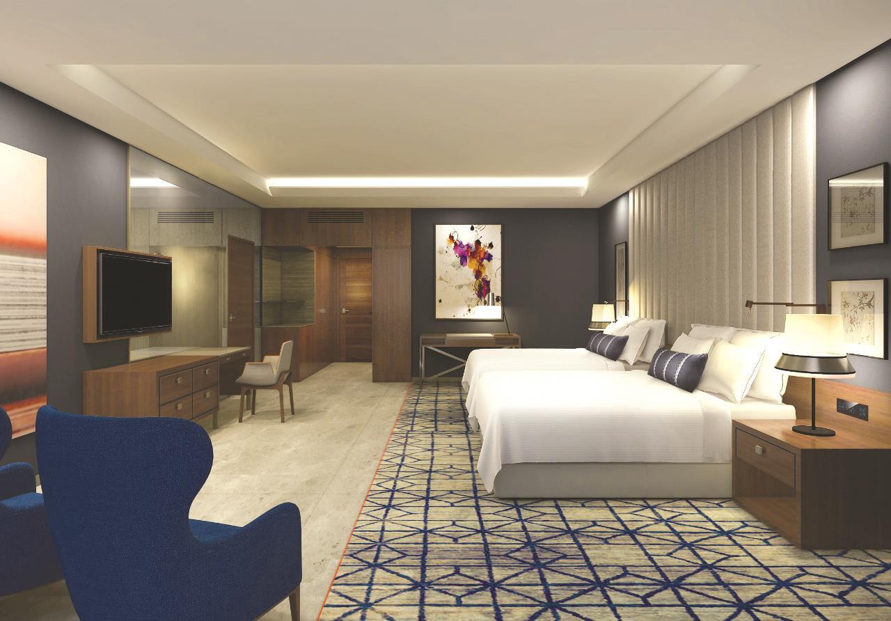โรงแรมแกรนด์ คอสโมโพลิตัน - ดูไบ ภายนอก รูปภาพ The image shows a modern hotel room featuring two beds with white linens. The room has a sleek design with a combination of blue, gray, and wooden accents. There is a large flat-screen TV mounted on the wall across from the beds. A blue armchair is p